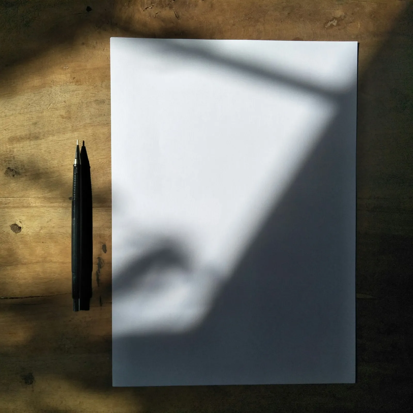 A blank sheet of paper and pens on a wooden desk
